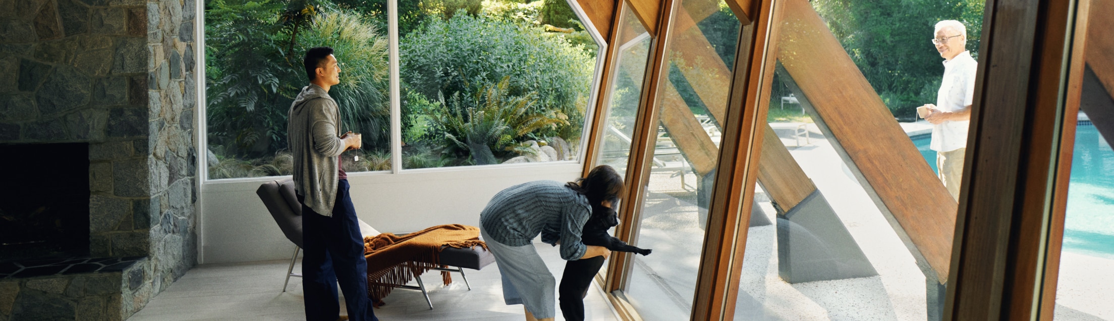 A man with a woman holding a dog looking out their vacation rental living room window at the outdoor pool area.